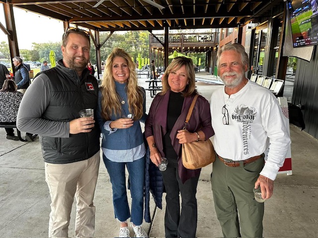 Group of four people standing under outdoor shelter.